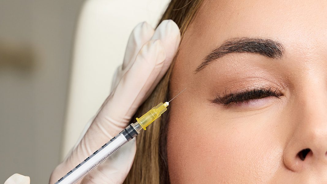Gloved injector placing Botox near the outer brow of a woman with closed eyes, the spot treated for a fox eye brow lift